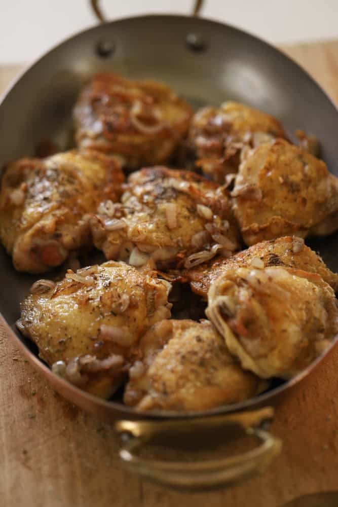 Crispy chicken thighs in a gratin pan with caramelized shallots on top.