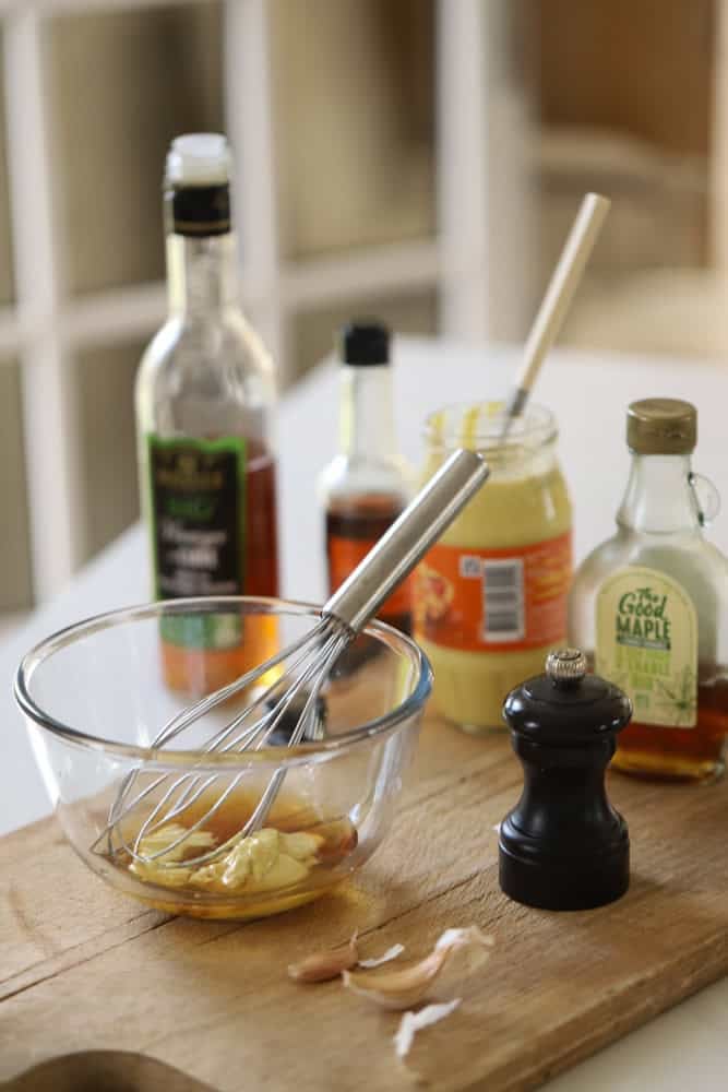 Ingredients for a maple Dijon sauce being mixed up on a counter in a small bowl with a whisk.