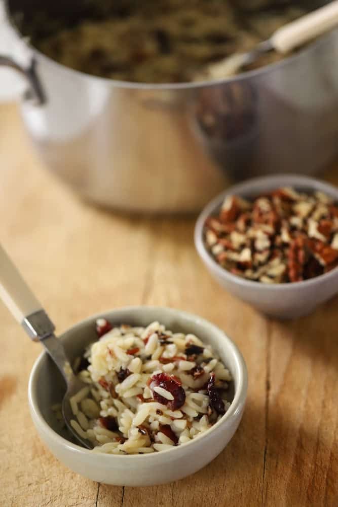 a small bowl of wild rice with plump cranberries and a bowl of pecans and rice pot in the background.