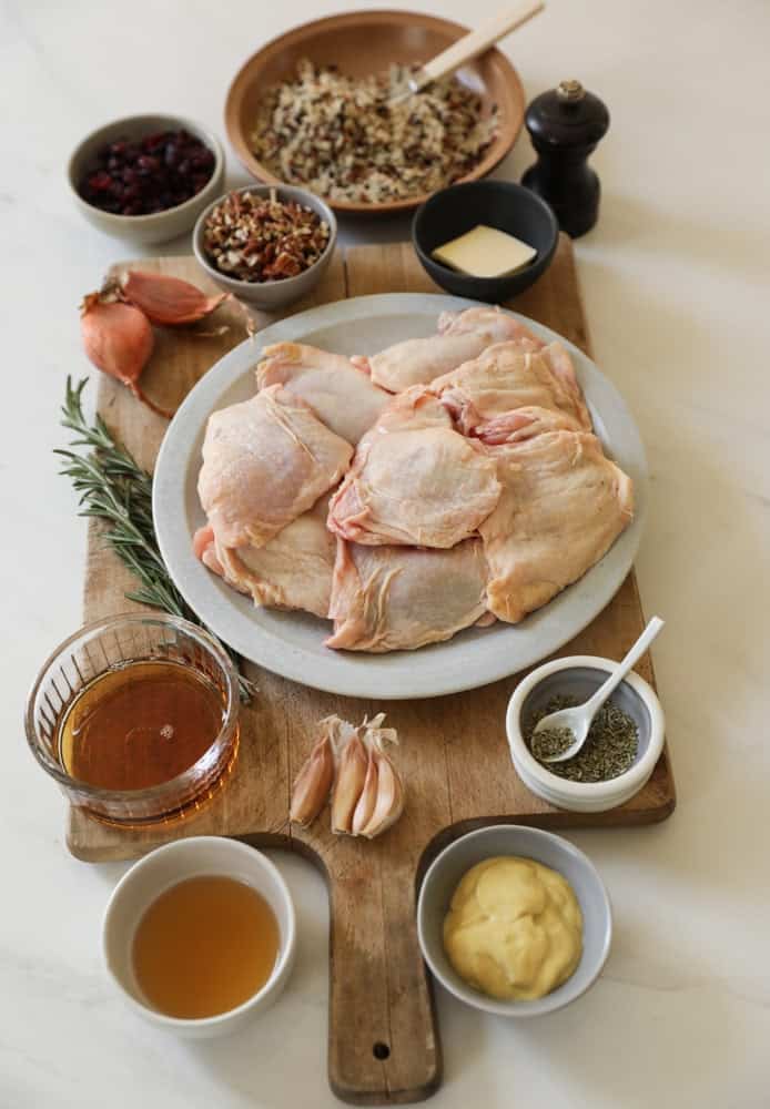 Chicken thighs on a plate with maple syrup, Dijon mustard, garlic, chicken broth, rosemary and seasonings.