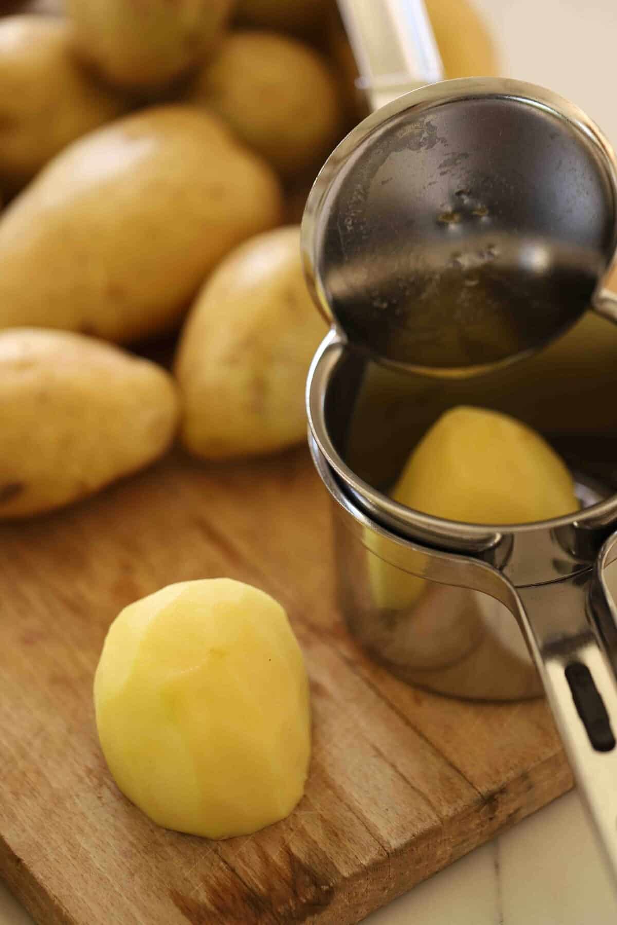 A peeled potato cut in half going into a ricer.
