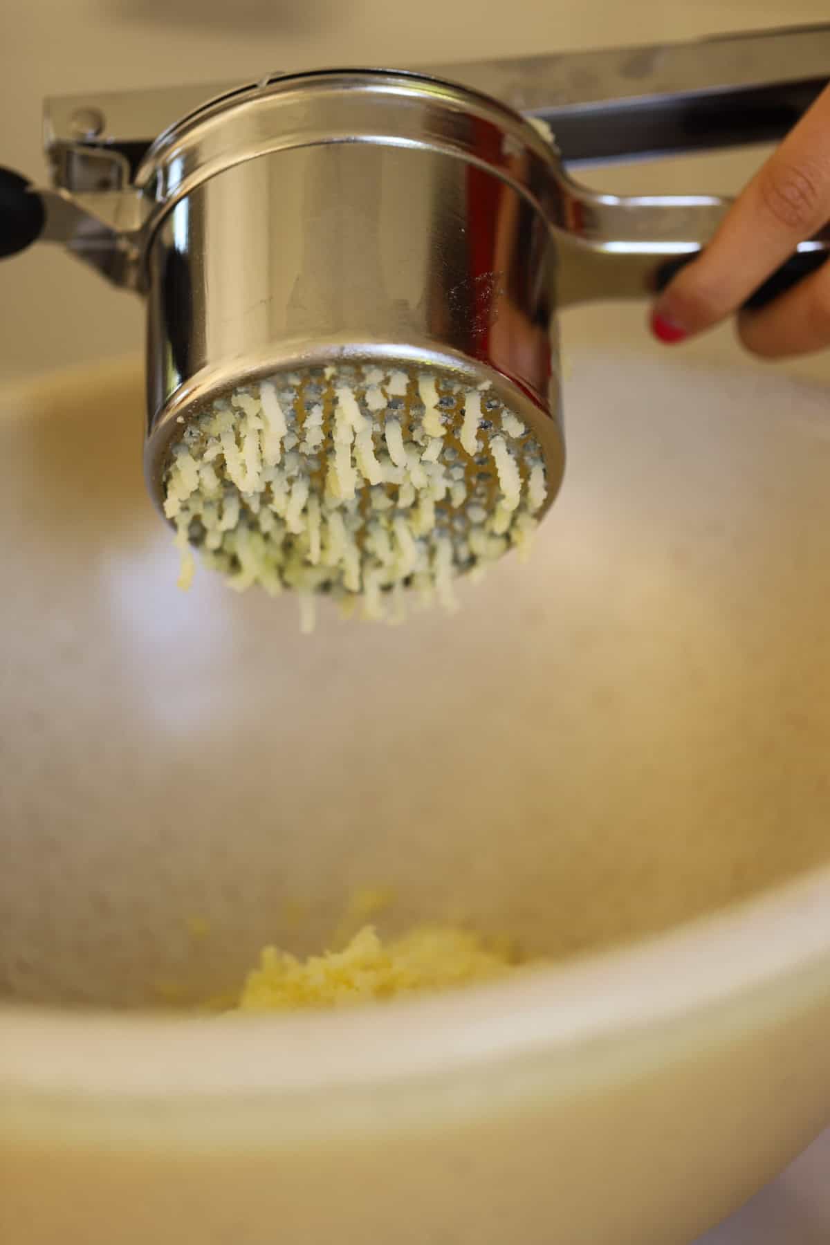 Potatoes being riced through a potato ricer into a bowl. 
