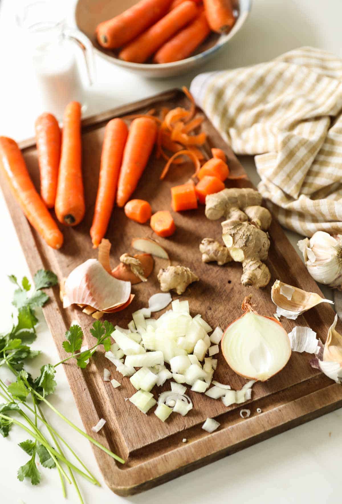Carrots, Onions, shallots and garlic being chopped on a cutting board.