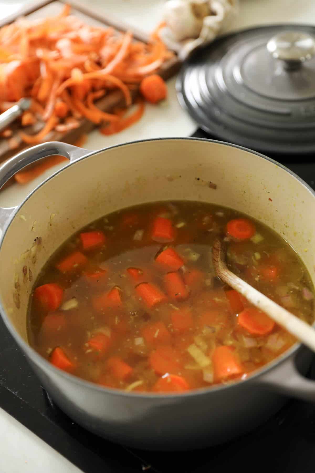 a large soup pot with vegetable broth, carrots and onions simmering.