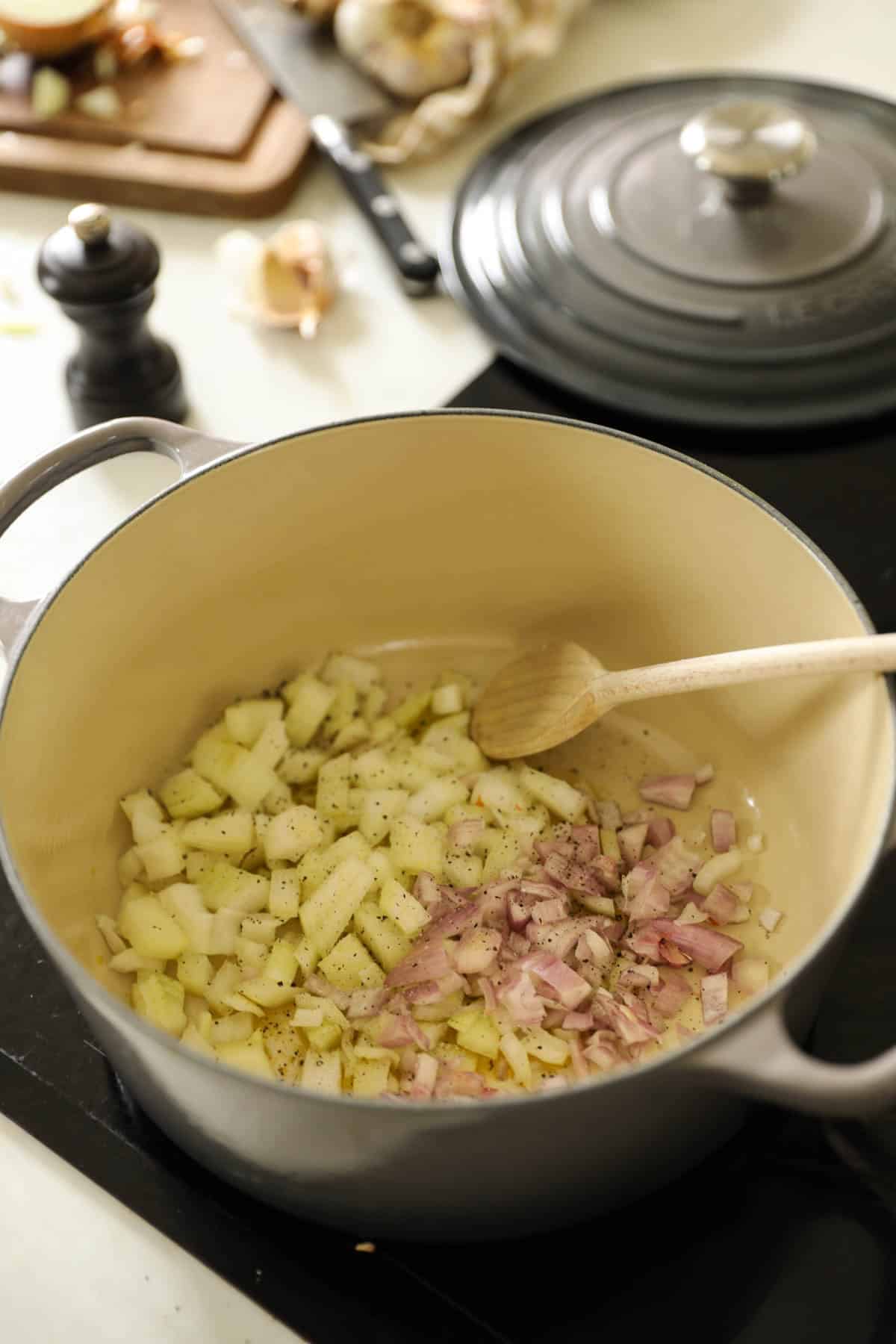 A large Dutch oven with carrots and shallots sautรฉing in olive oil.