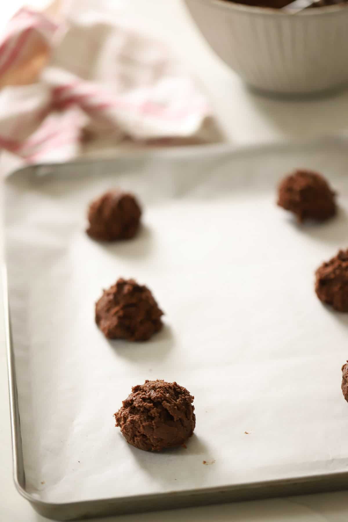 Cookie dough balls on a cookie sheet lined with parchment paper.
