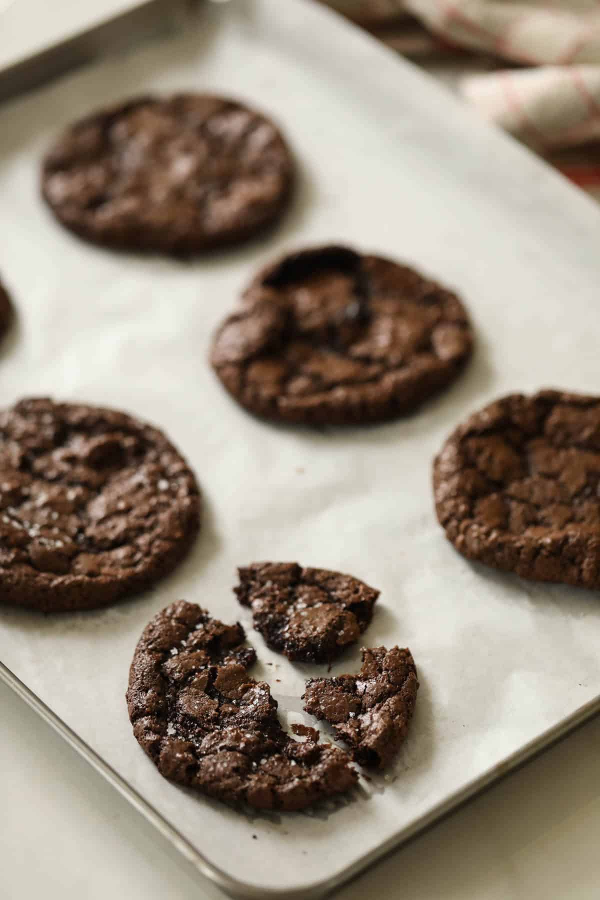A broken fudgy brownie cookie on a parchment lined cookie sheet.