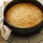 A cake cooling on a cake stand in a cheesecake pan.