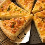 A quiche cut into slices with a silver pie server serving a slice.