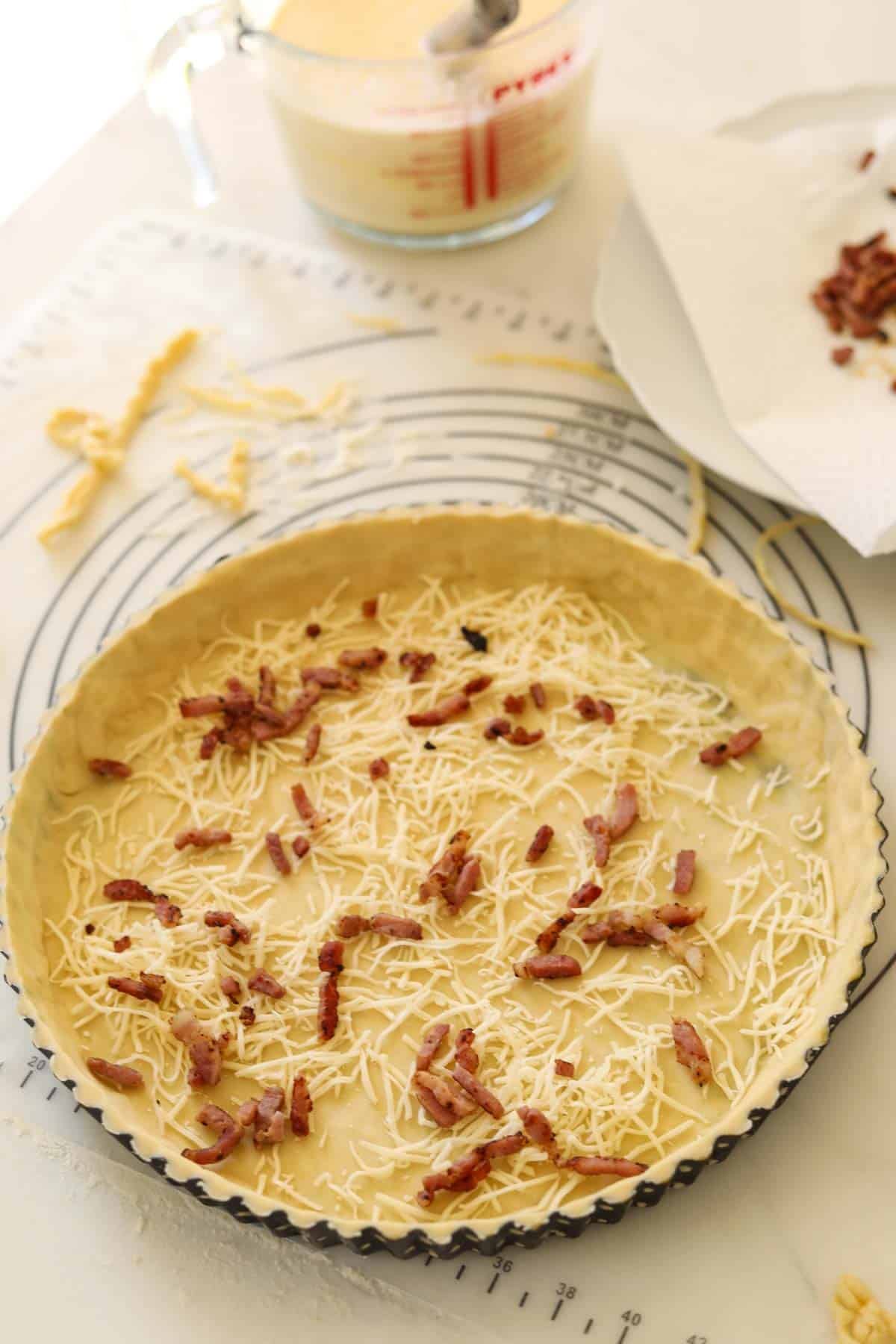 cheese and cooked bacon added to the bottom of a quiche pan crust.