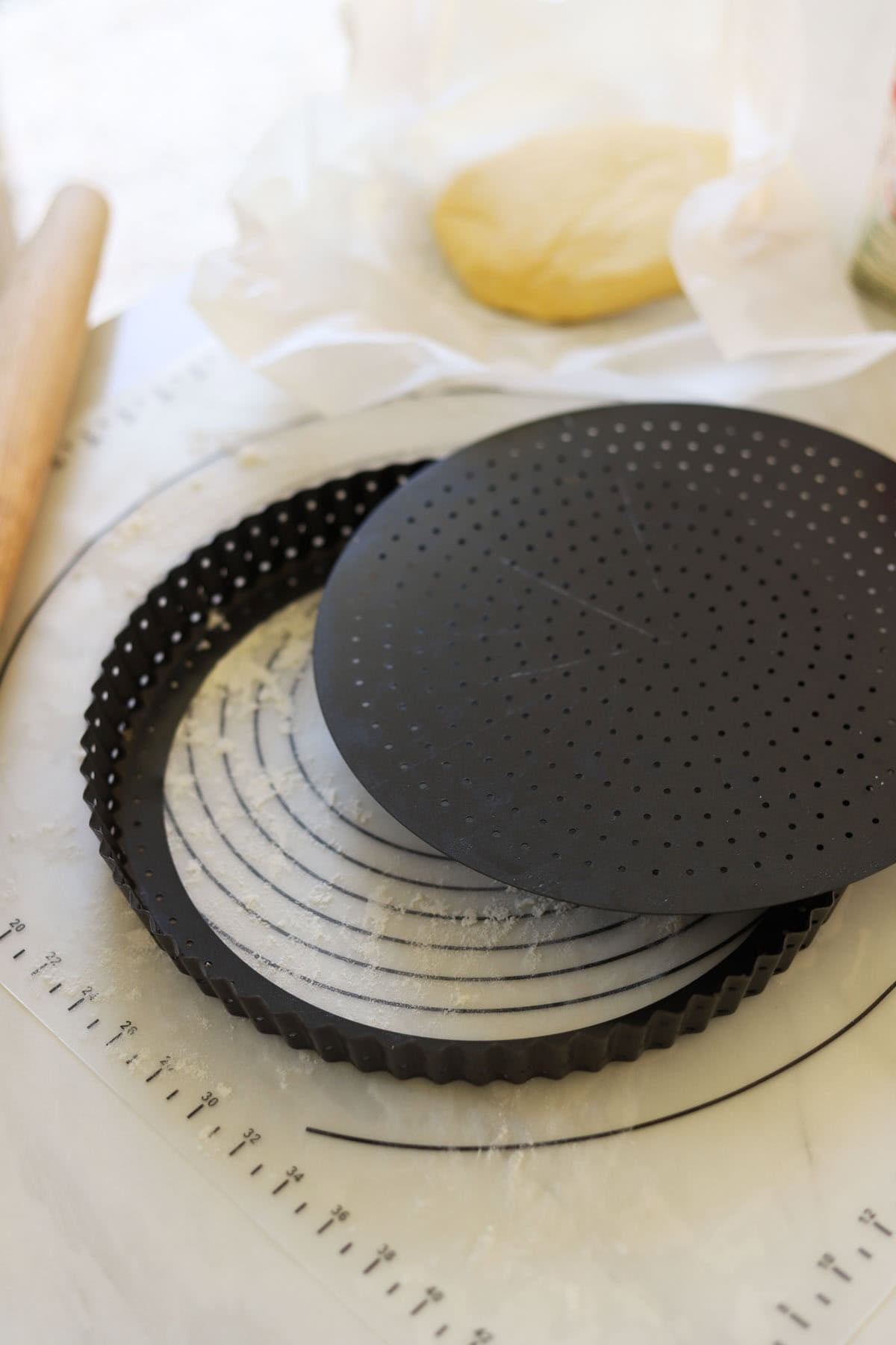 A removable bottom quiche pan and a disk of tart dough in the background.