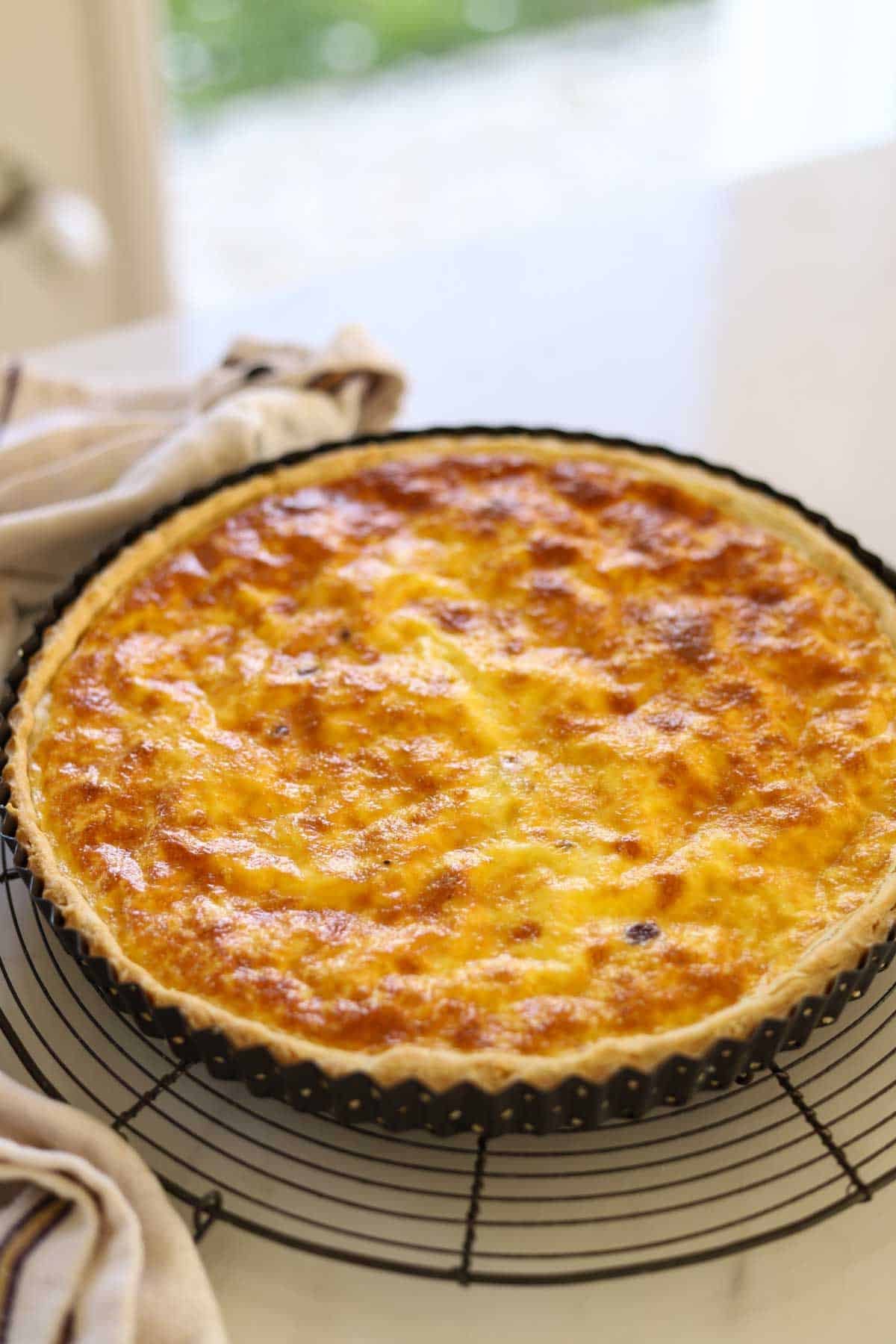 a quiche cooling on a wire rack with dish towel.