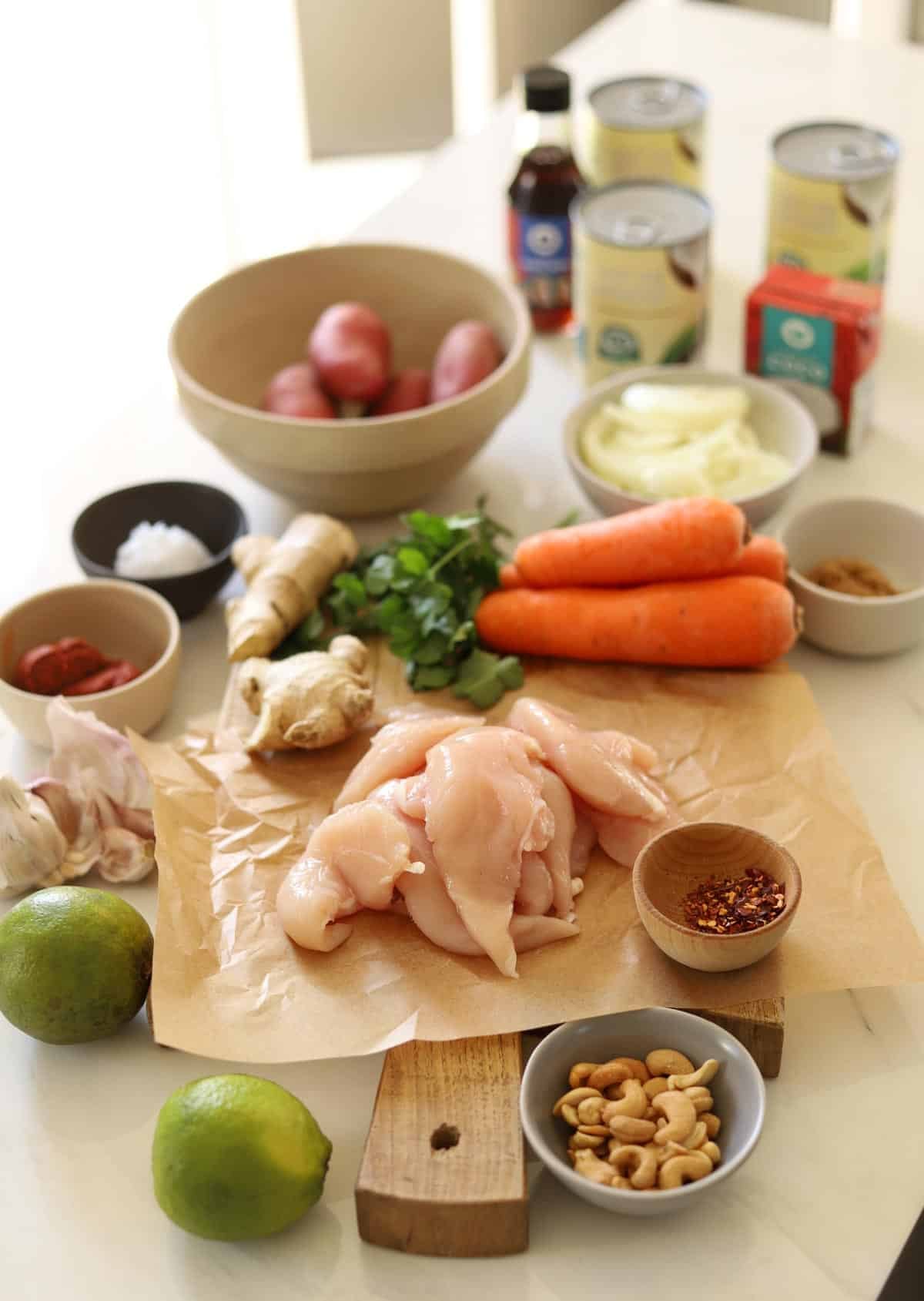 Chicken, carrots, potatoes and red curry paste laid out on a counter.