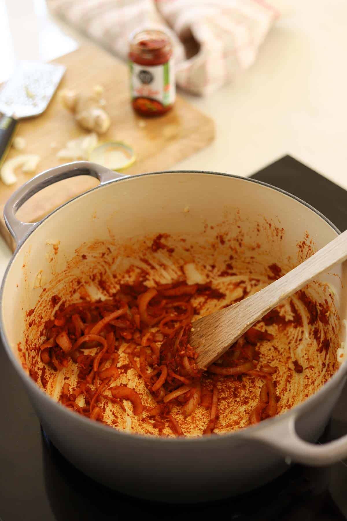 A dutch oven filled with onions, ginger, garlic and red curry paste.