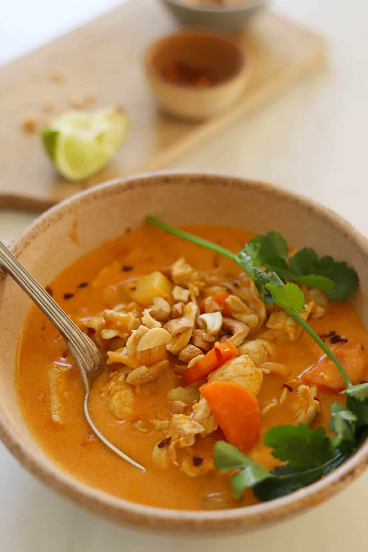 A bowl of Thai curry in a beige bowl with cilantro.