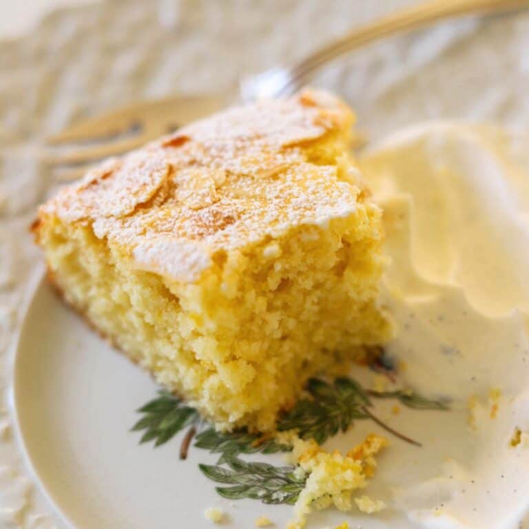 A half eaten slice of lemon cake on a plate with whipped cream.