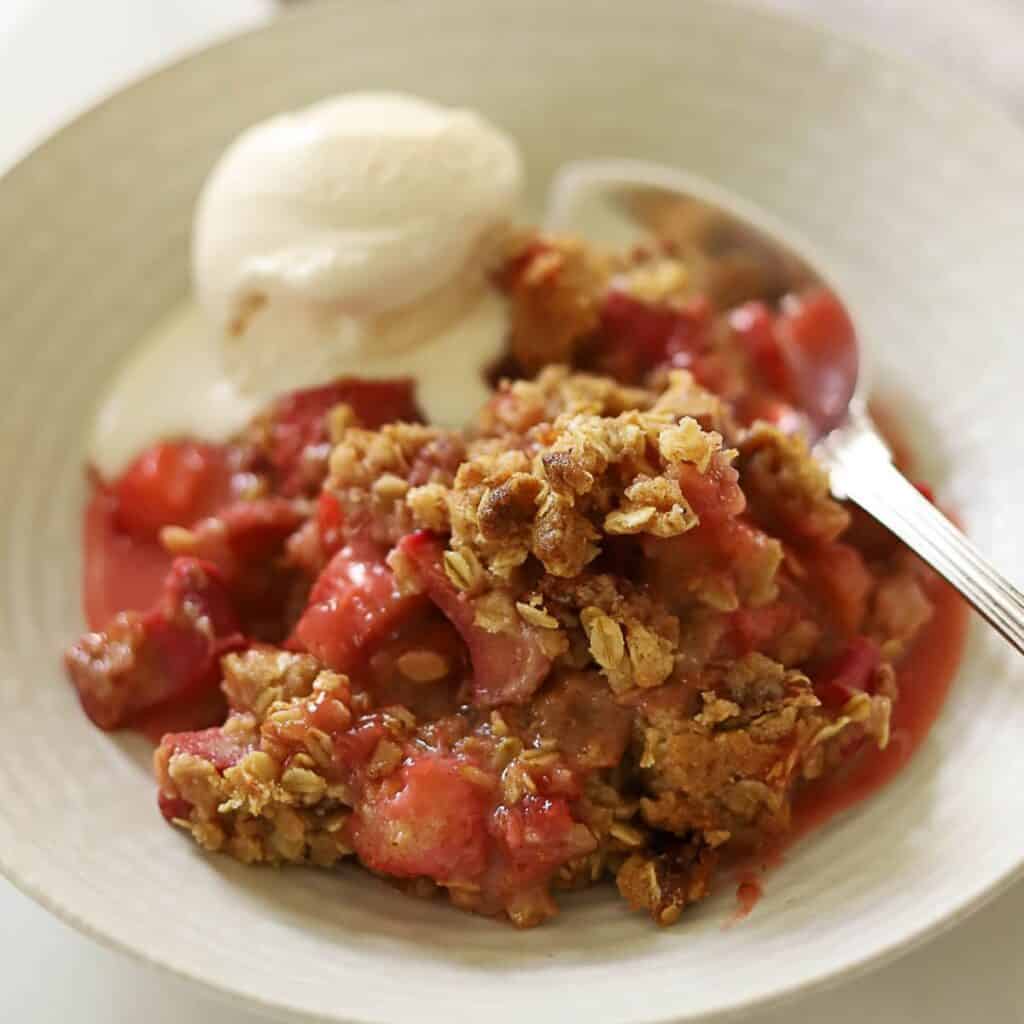a bowl of strawberry rhubarb crips with vanilla ice cream.